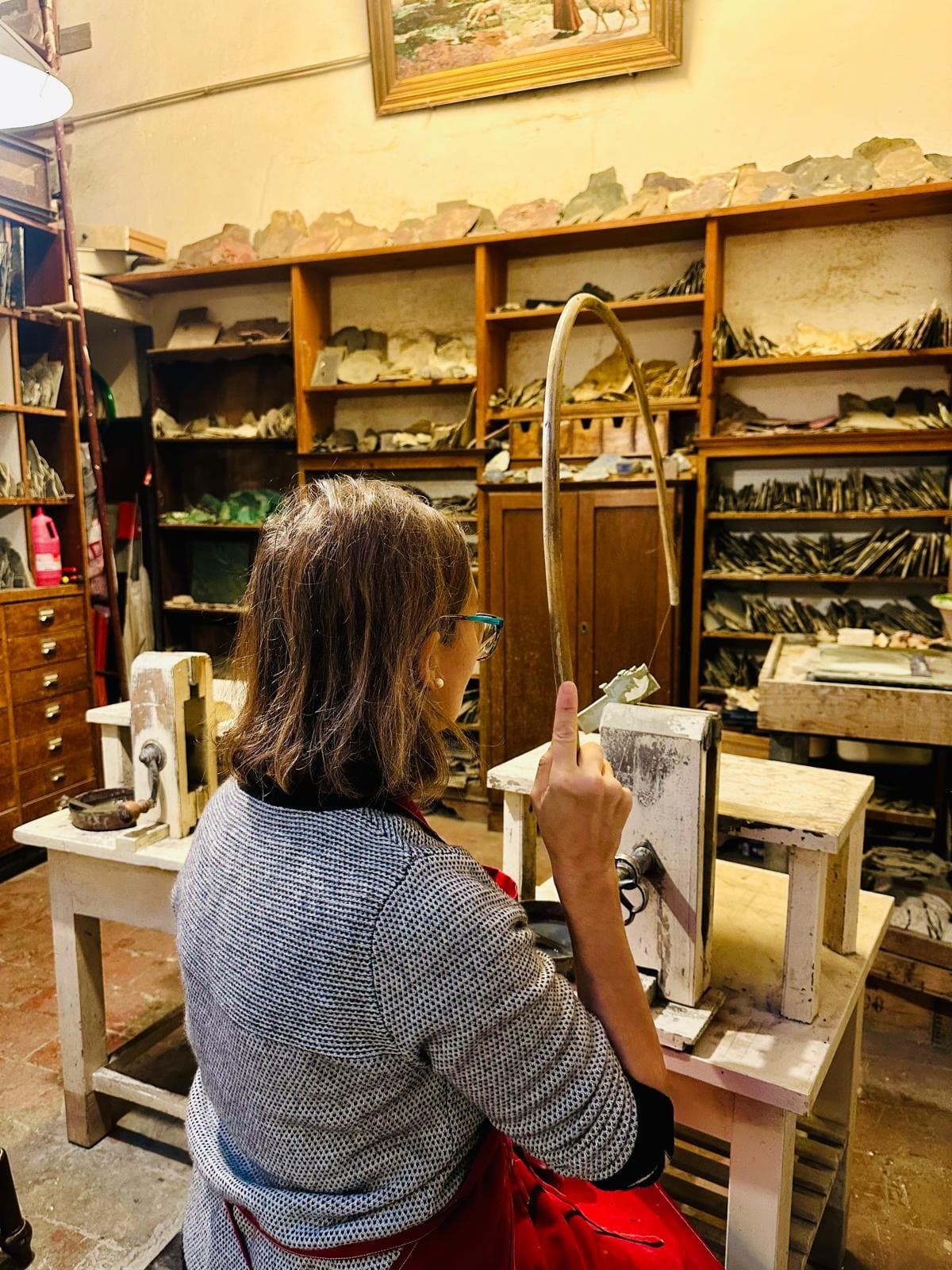 An artisan at the bench in a Florence workshop, shelves of stone and tools behind her