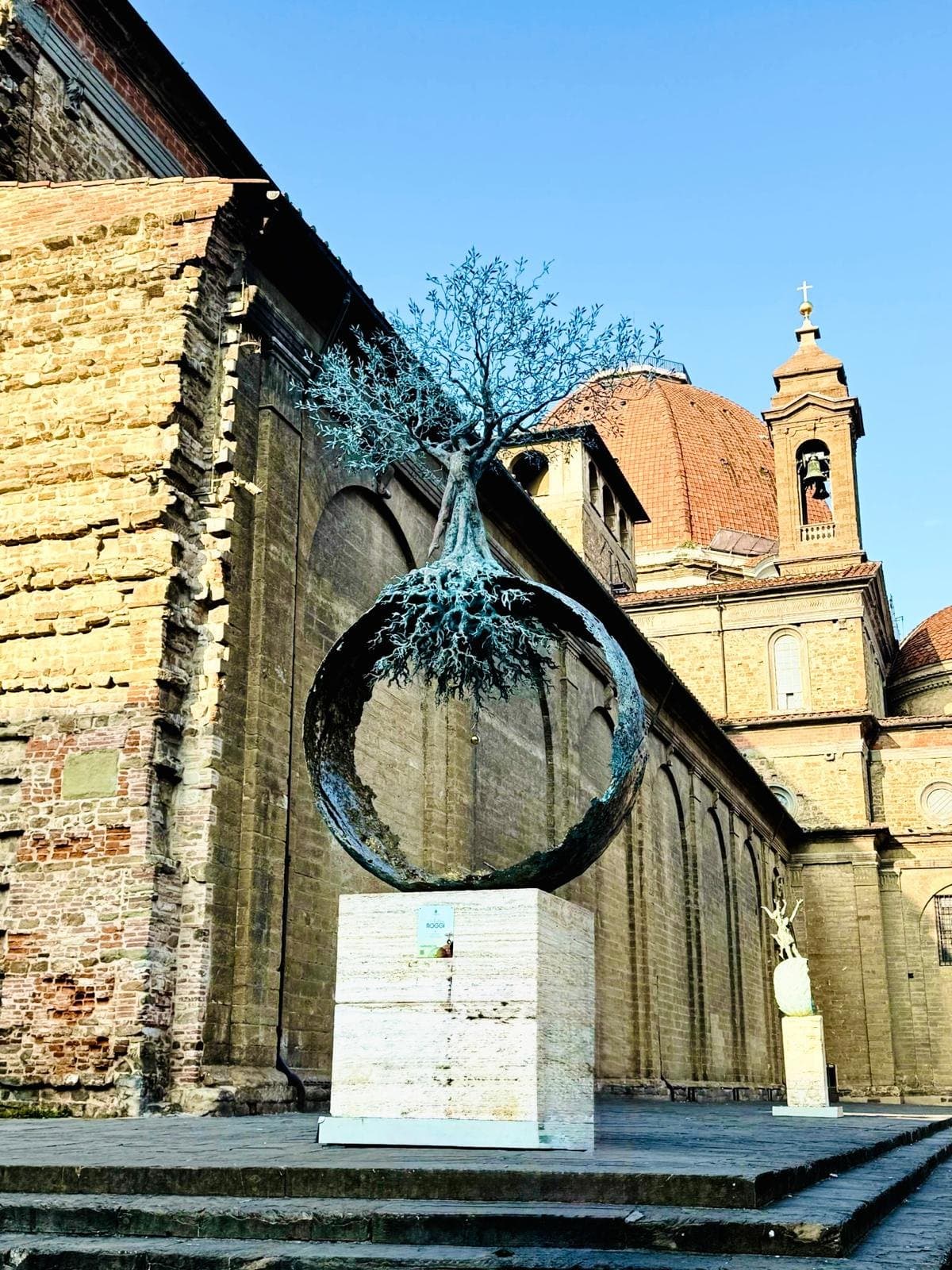 A bronze tree sculpture rooted in a sphere outside the Basilica of San Lorenzo