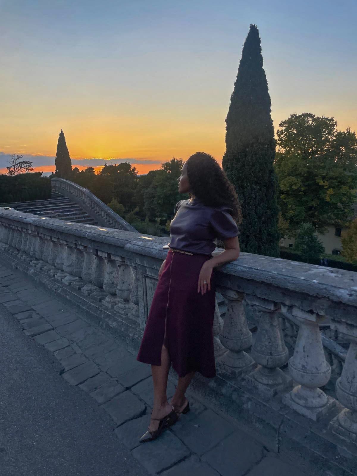 Kerry-Ann Stephens on a stone terrace at sunset, cypress trees along the balustrade