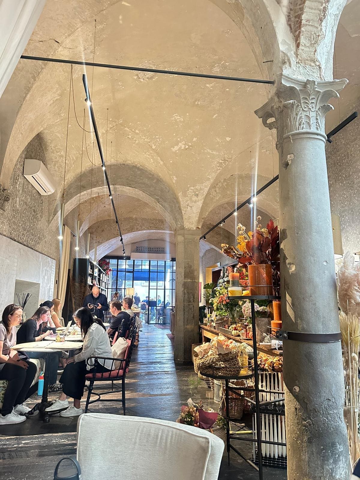 A vaulted Florence cafe with stone columns, flowers and tables along one side