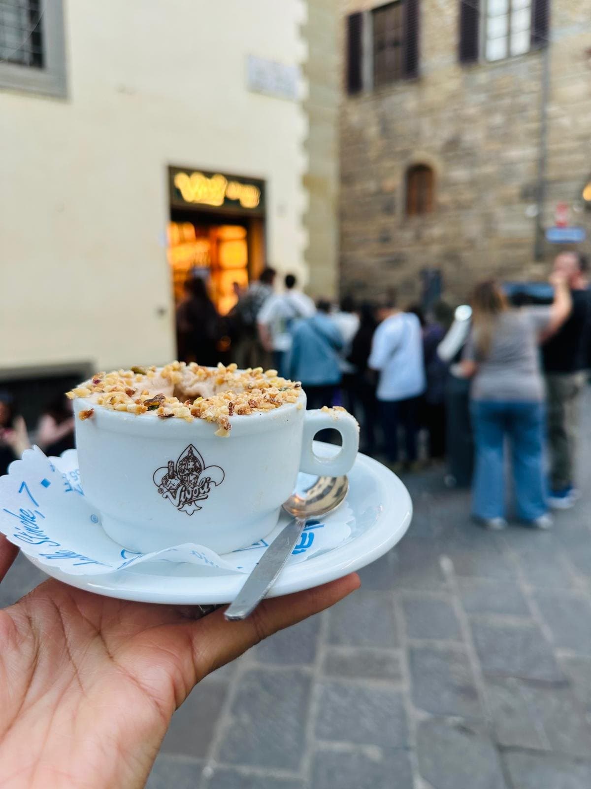 A cappuccino topped with chopped nuts held up in a Florence square