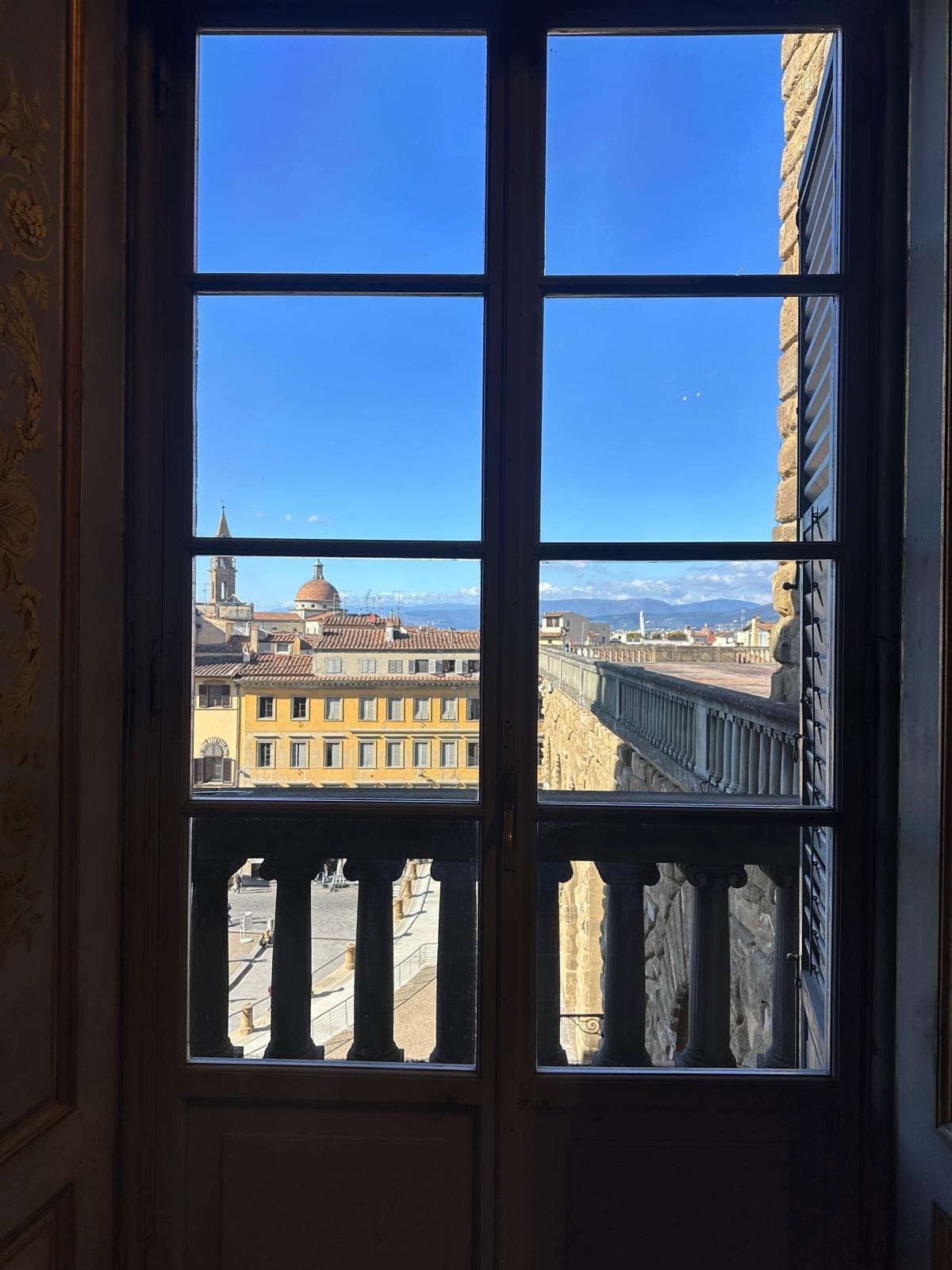Florence rooftops and a dome seen through a tall shuttered window