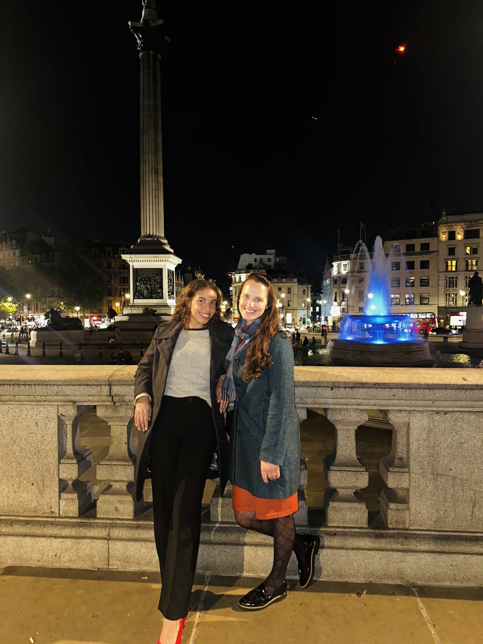 Two travelers by the fountains in Trafalgar Square at night