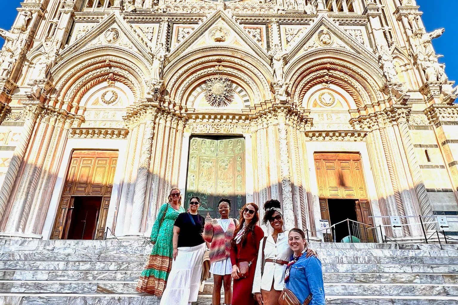 A group of women on the steps of Siena cathedral beneath its striped marble facade