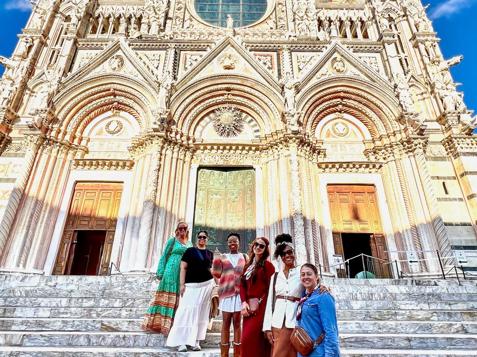A group of women on the steps of Siena cathedral beneath its striped marble facade