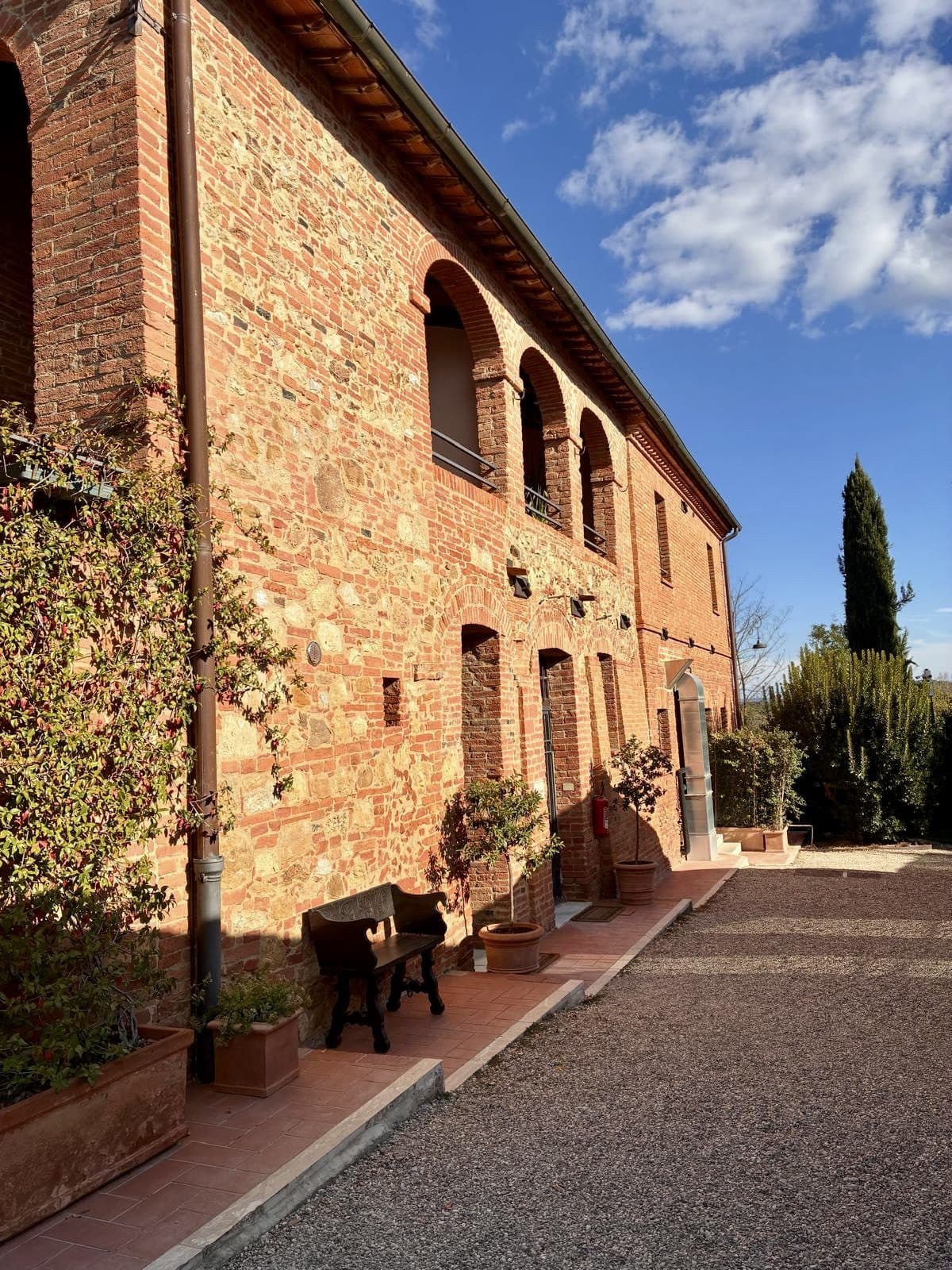 A stone Tuscan farmhouse with a terracotta roof and cypress trees beside it