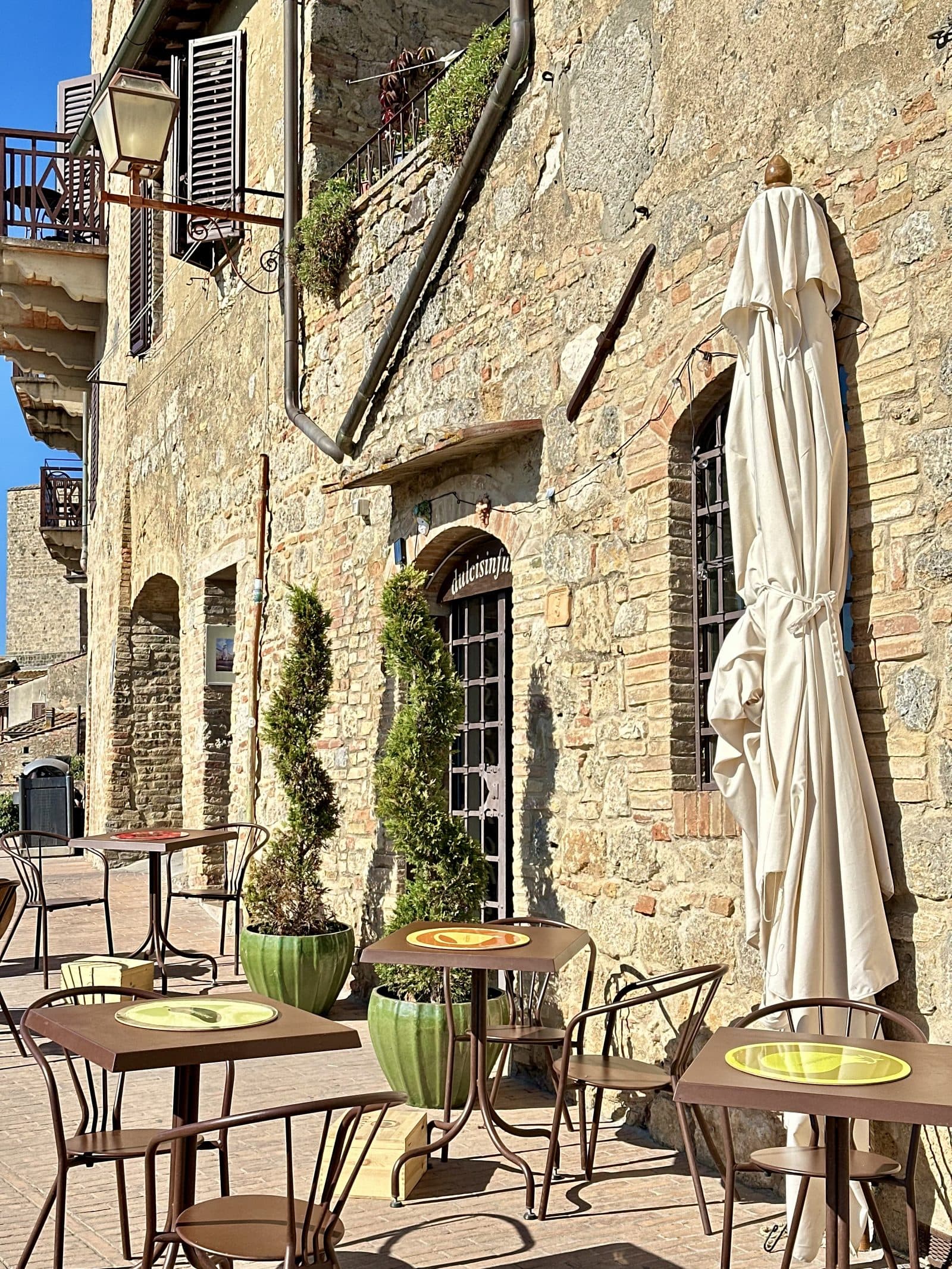 Cafe tables and closed umbrellas on a stone street in a Tuscan hill village