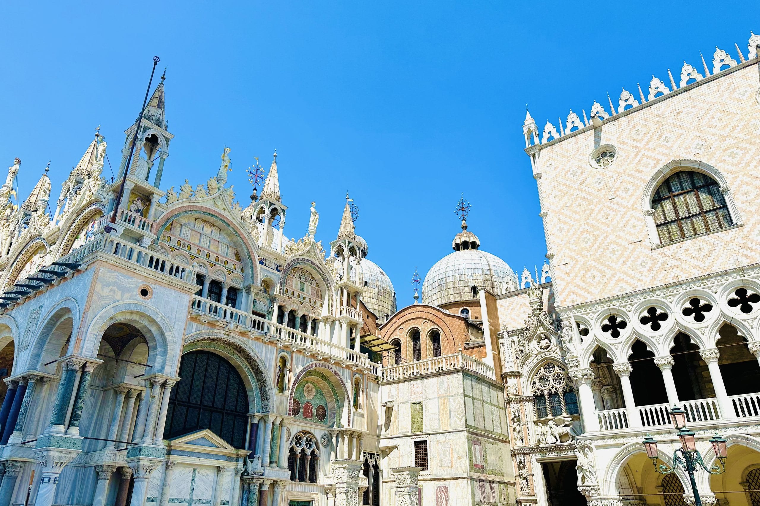The carved facade of St Mark's Basilica beside the Doge's Palace under a clear blue sky