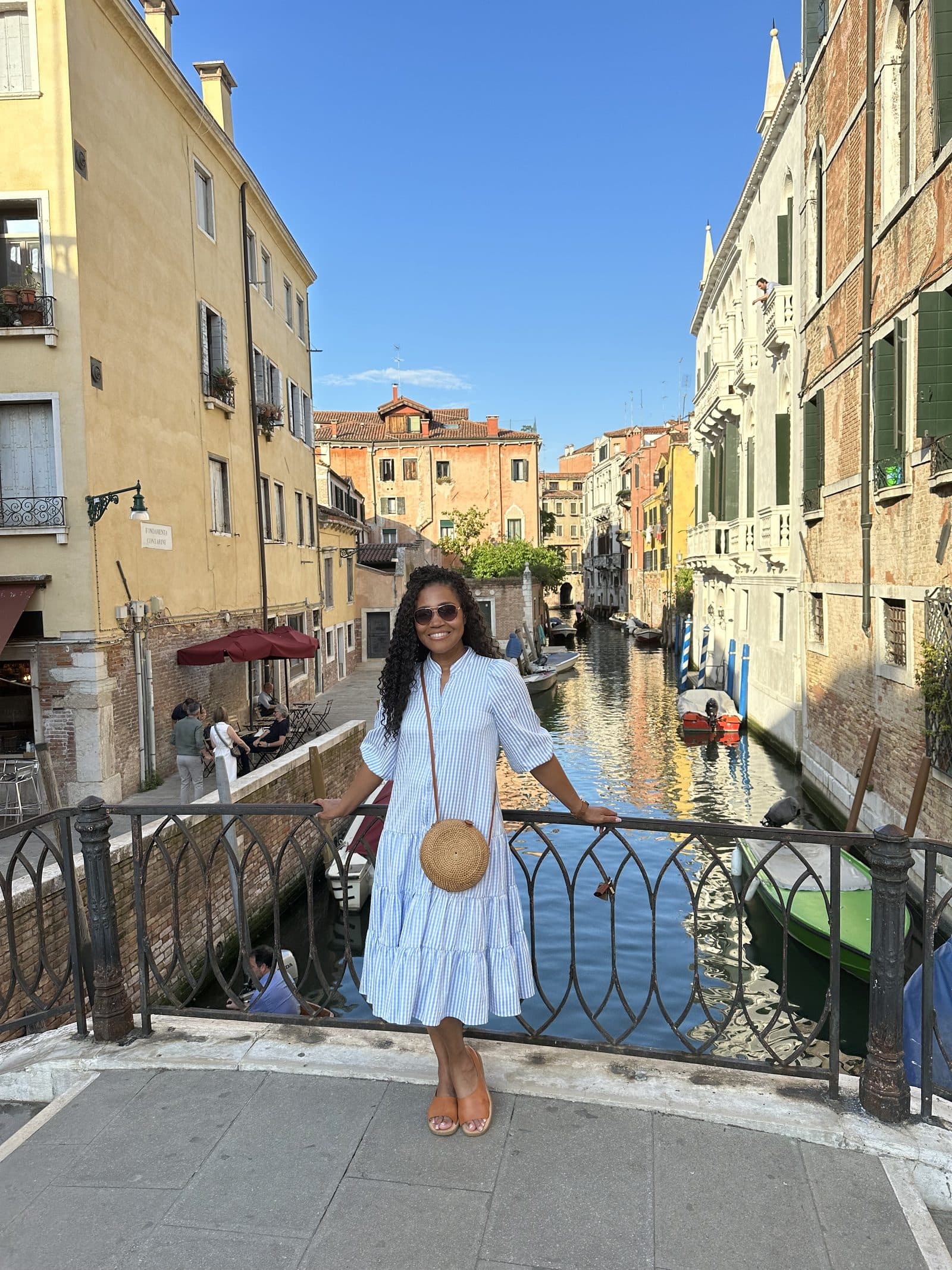 A traveler standing on a bridge over a Venetian canal lined with pastel buildings