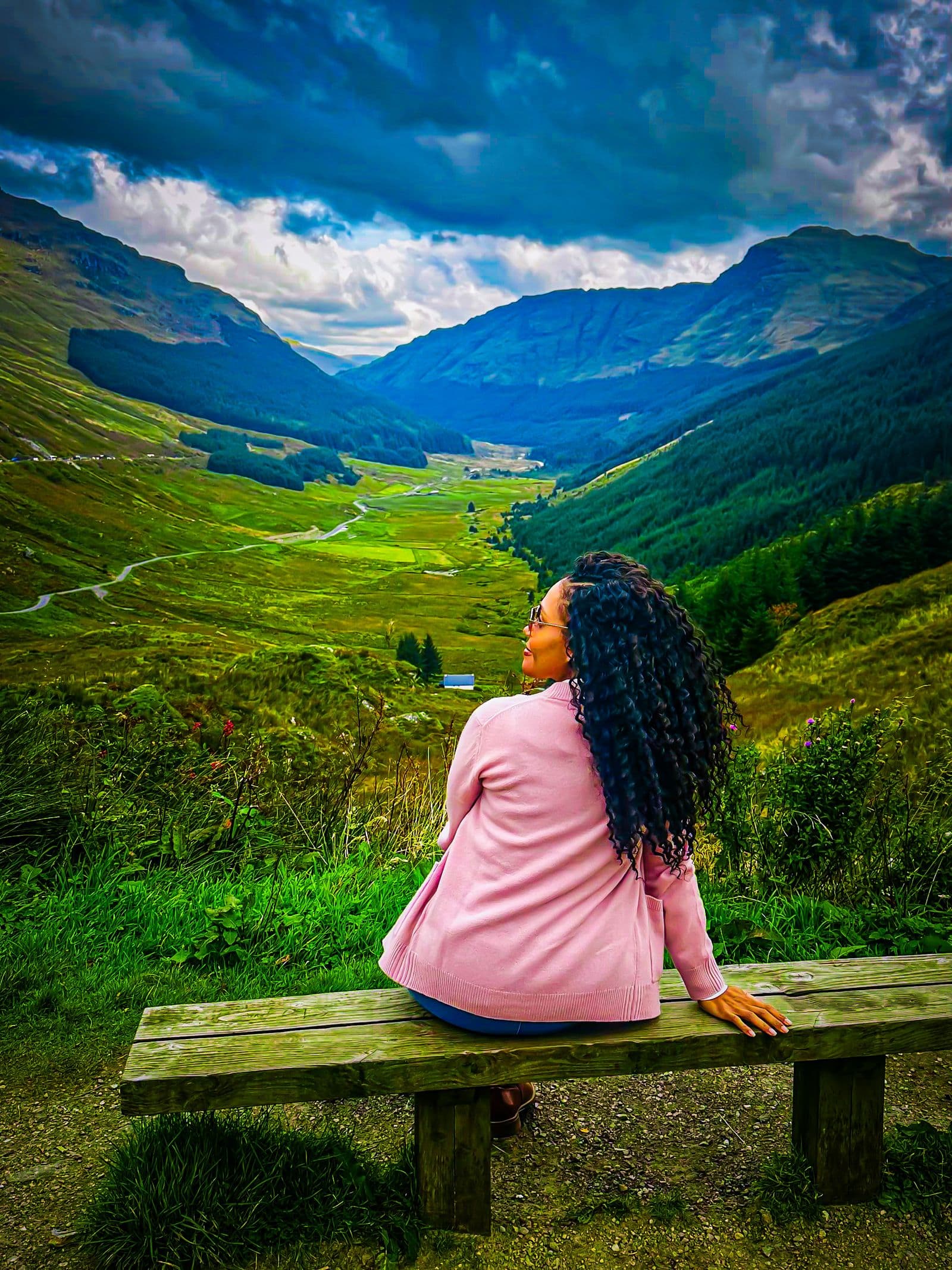 Kerry-Ann Stephens sitting on a wooden bench looking out over a green Highland valley