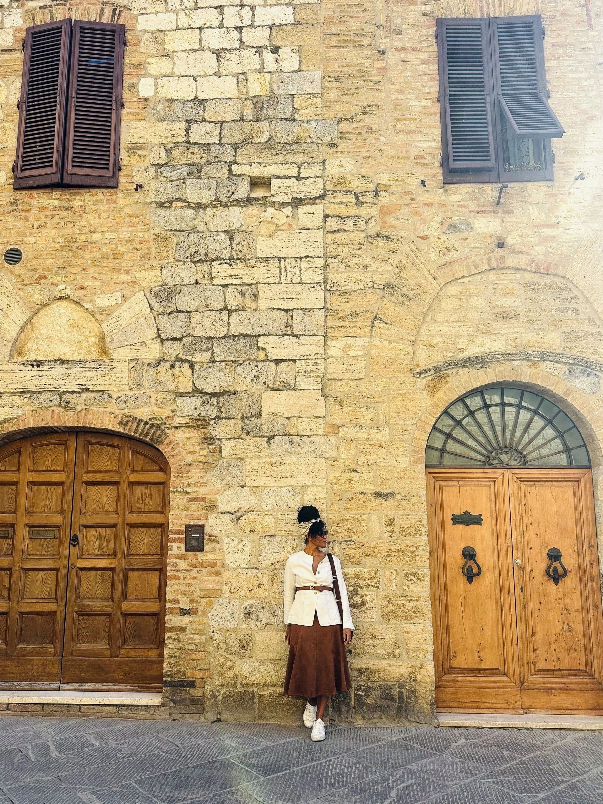 Kerry-Ann Stephens standing against a medieval stone wall between two wooden doors in San Gimignano, Tuscany