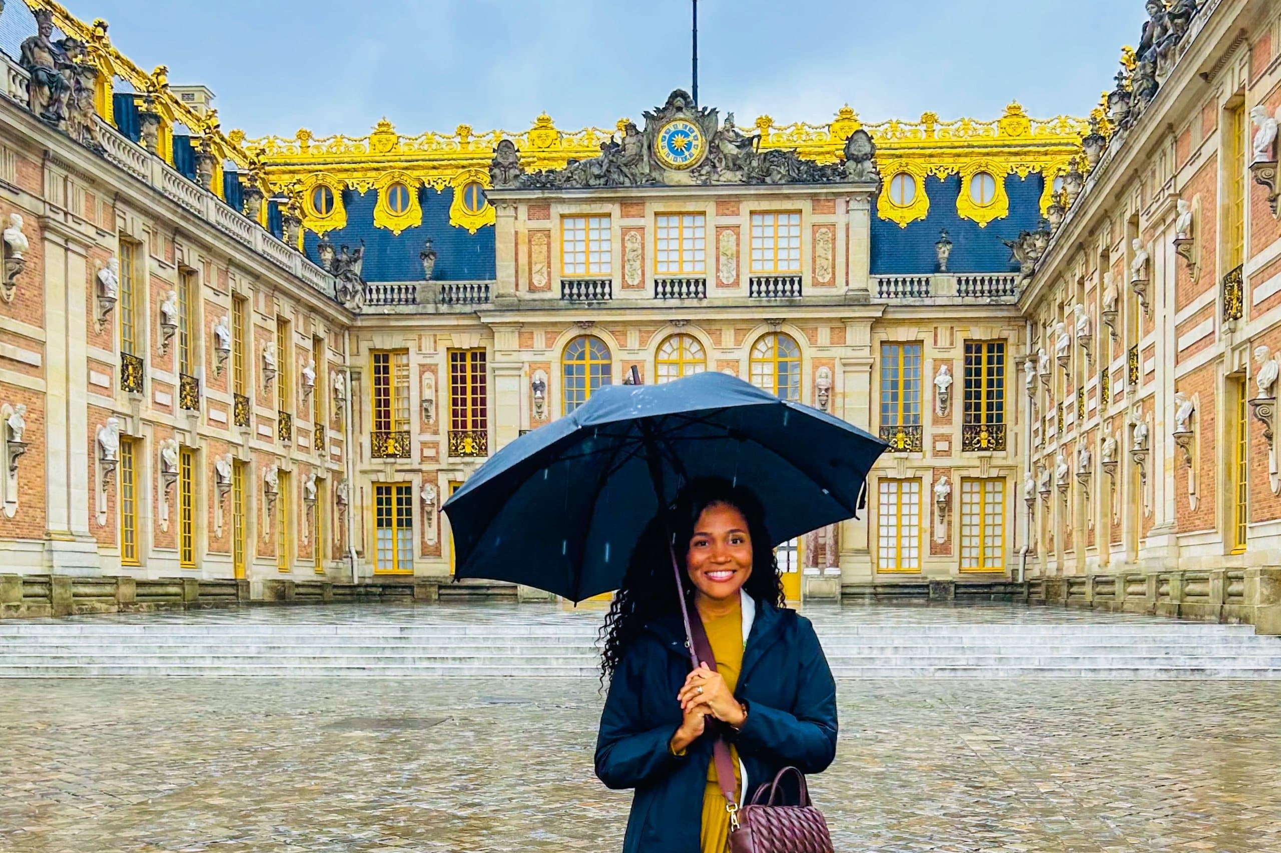 The gilded forecourt of the Château de Versailles in the rain, a single figure with an umbrella