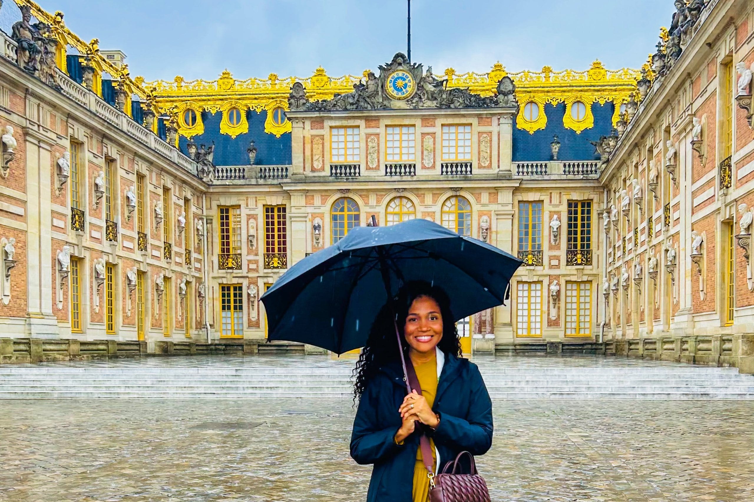 The gilded forecourt of the Château de Versailles in the rain, a single figure with an umbrella