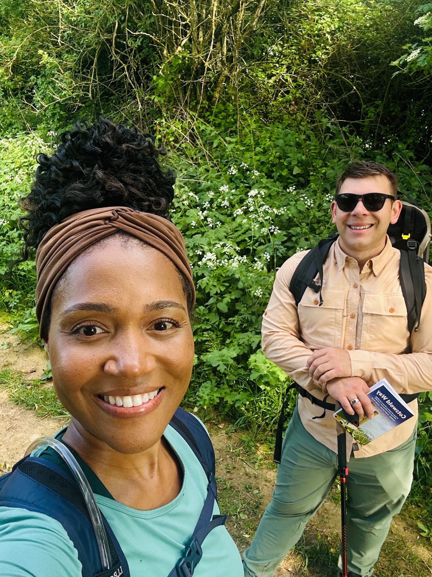 Two walkers with backpacks on a green path between hedgerows