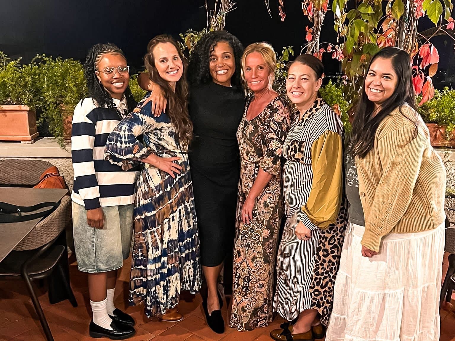 A group of women together at a retreat dinner under a vine-covered terrace