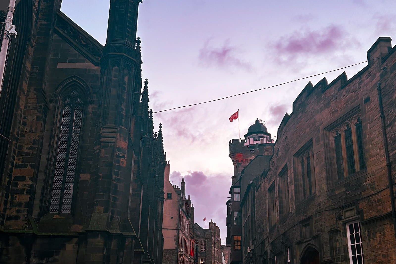 The Royal Mile at dusk, empty cobbles running between old stone buildings under a violet sky