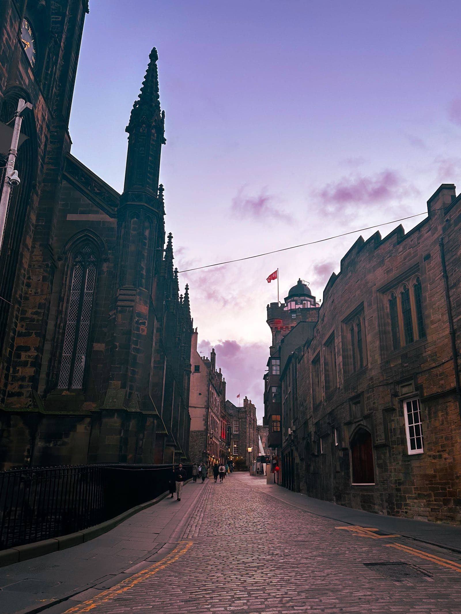 The Royal Mile in Edinburgh at dusk, empty cobbles running down between old stone buildings under a violet sky