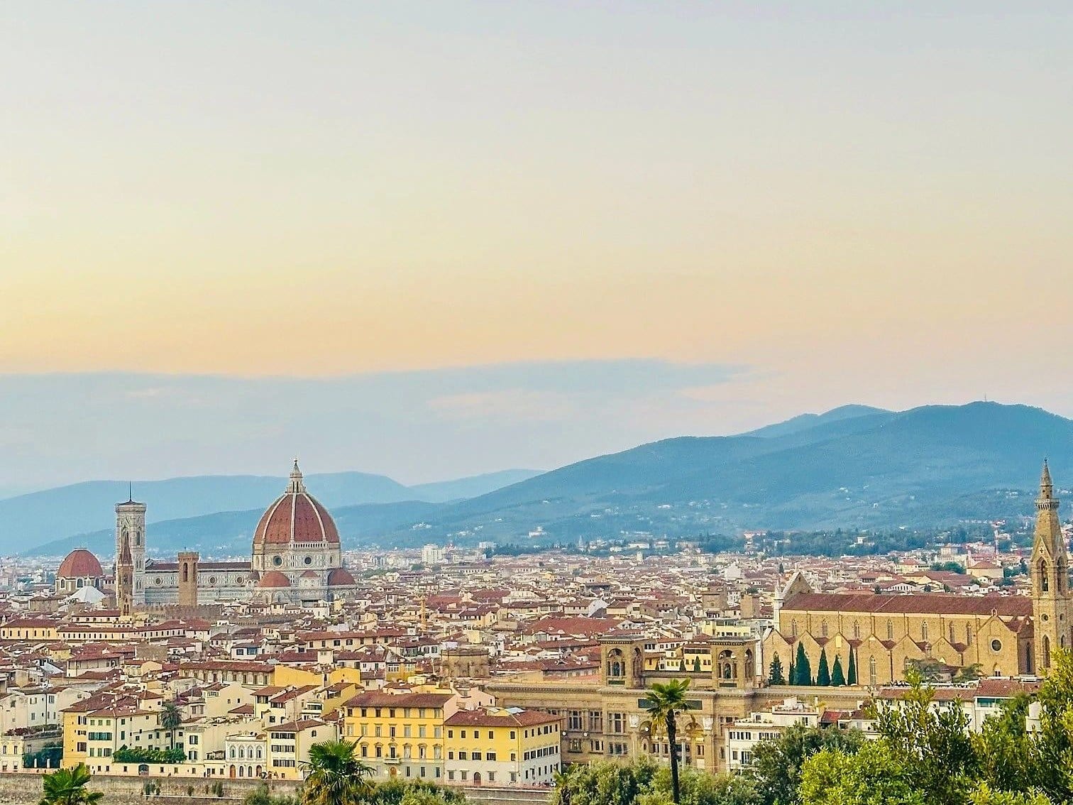 Florence at sunset seen across the whole city, the Duomo and Santa Croce among the rooftops with the Tuscan hills beyond