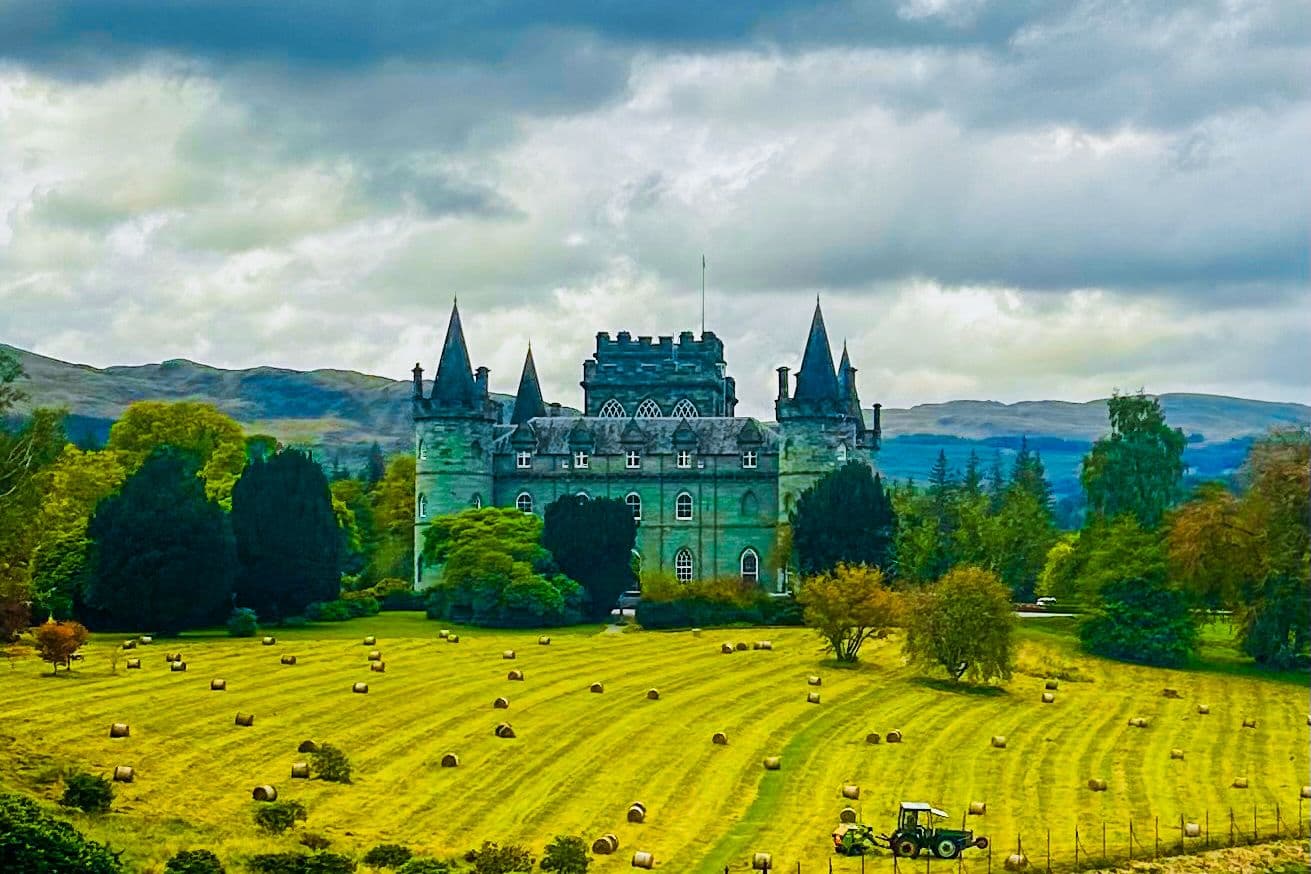 Inveraray Castle across a mown hayfield of round bales, with the Argyll hills behind