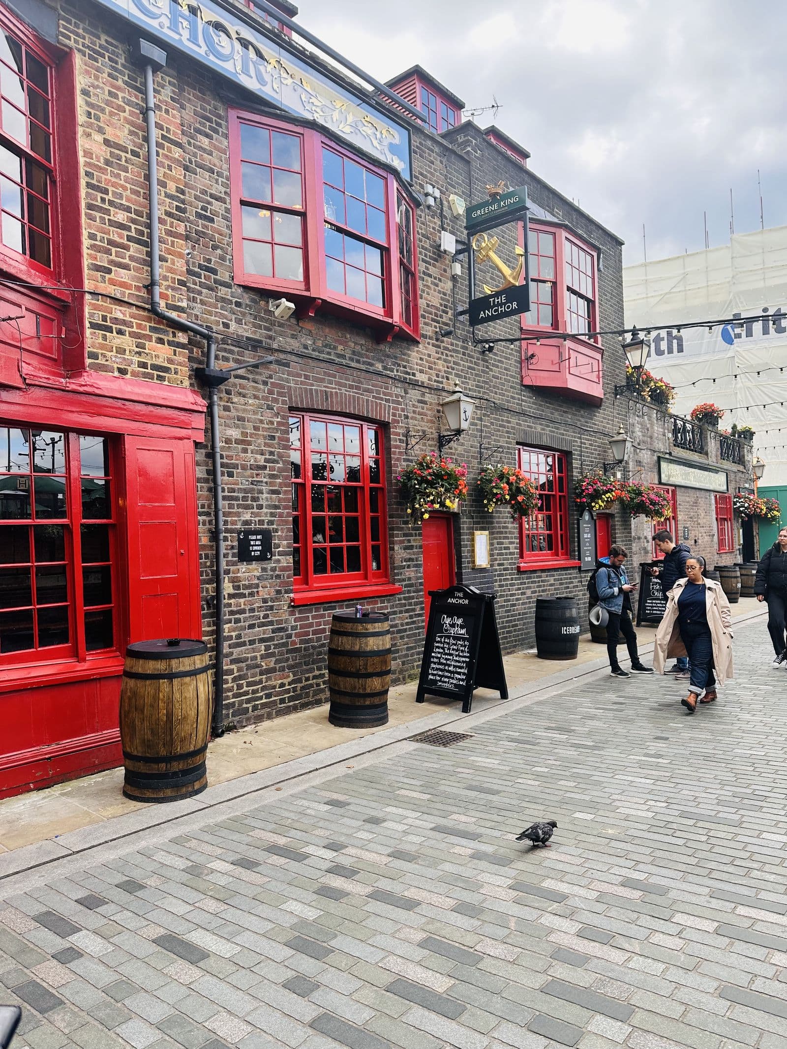 A red-painted London pub with barrels and blackboards on the pavement outside