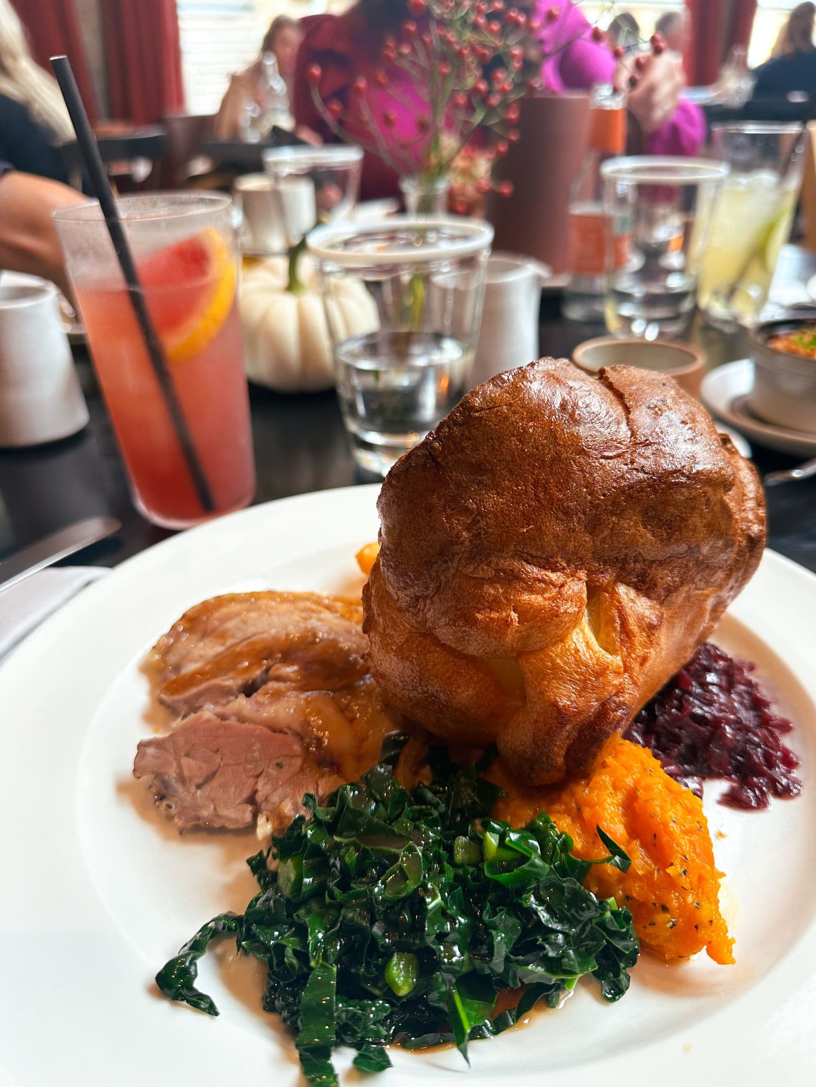 A Sunday roast with a tall Yorkshire pudding and greens on a pub table