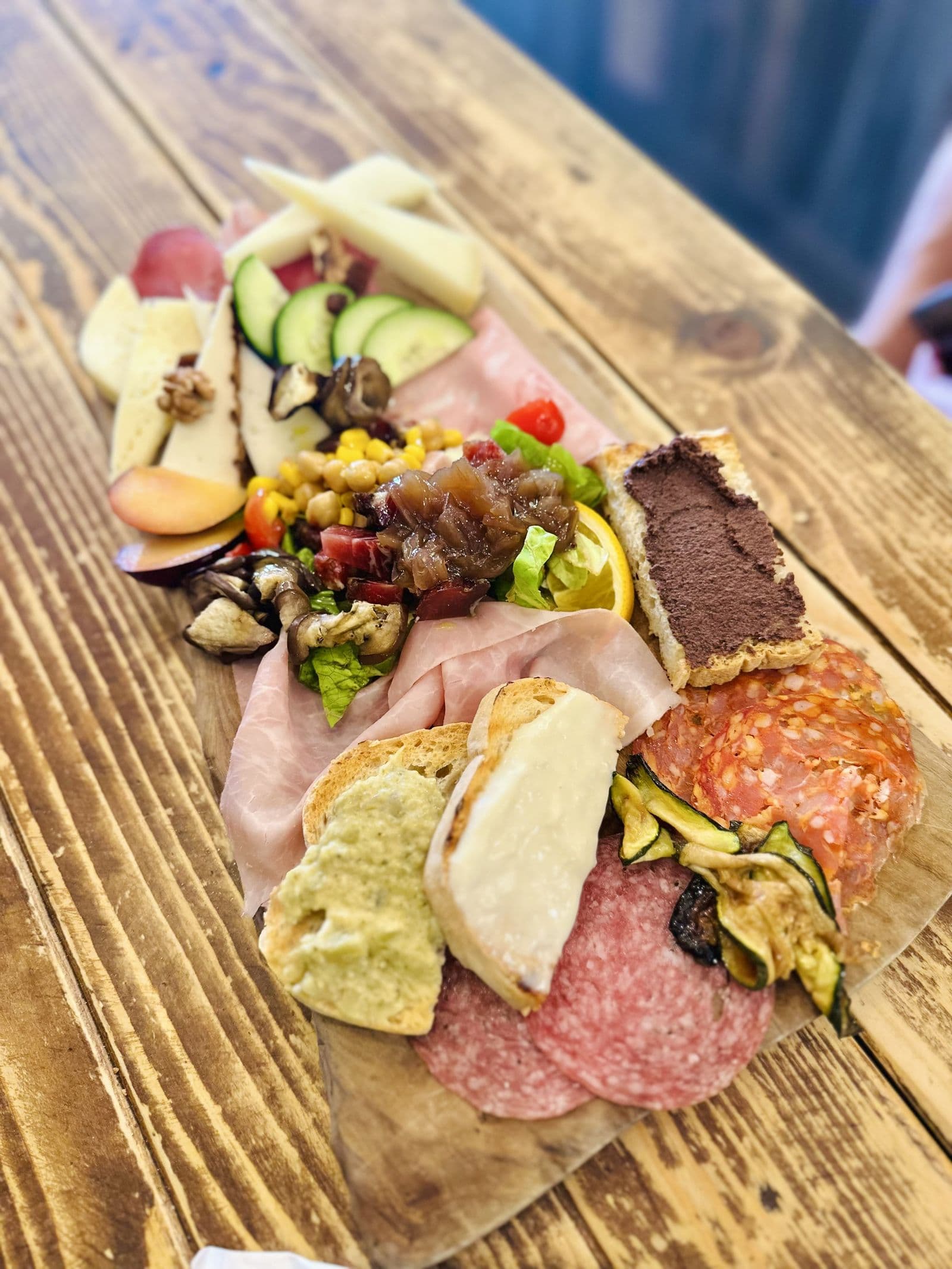 A wooden board of cured meats, cheeses and vegetables on a restaurant table