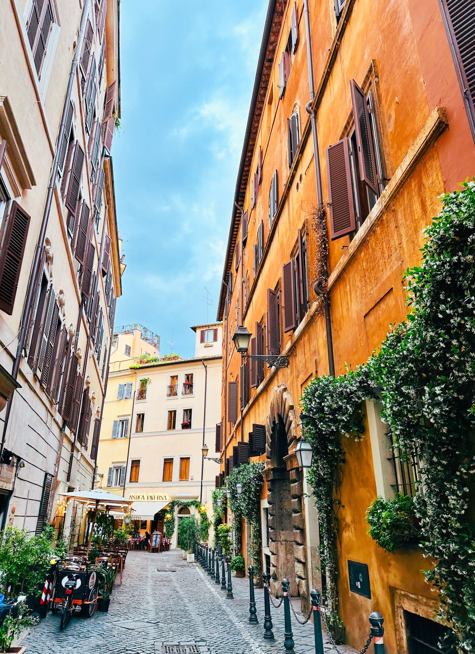 A narrow Roman back street of ochre buildings with shuttered windows and parked scooters