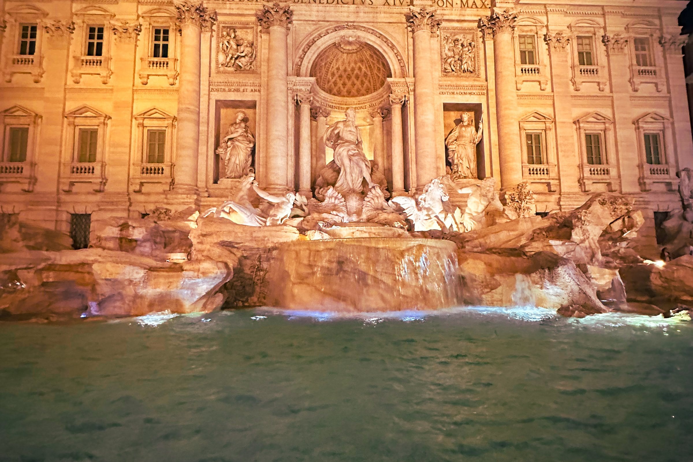 The Trevi Fountain lit at night, its sculpted figures glowing above the water