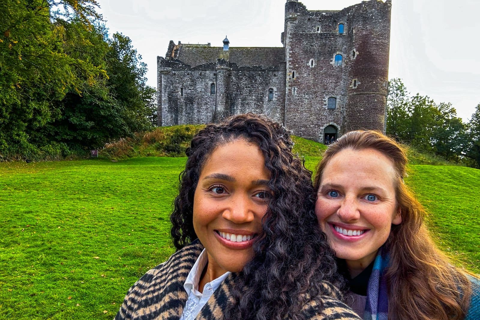 Doune Castle rising above its lawn, with two travelers in the foreground