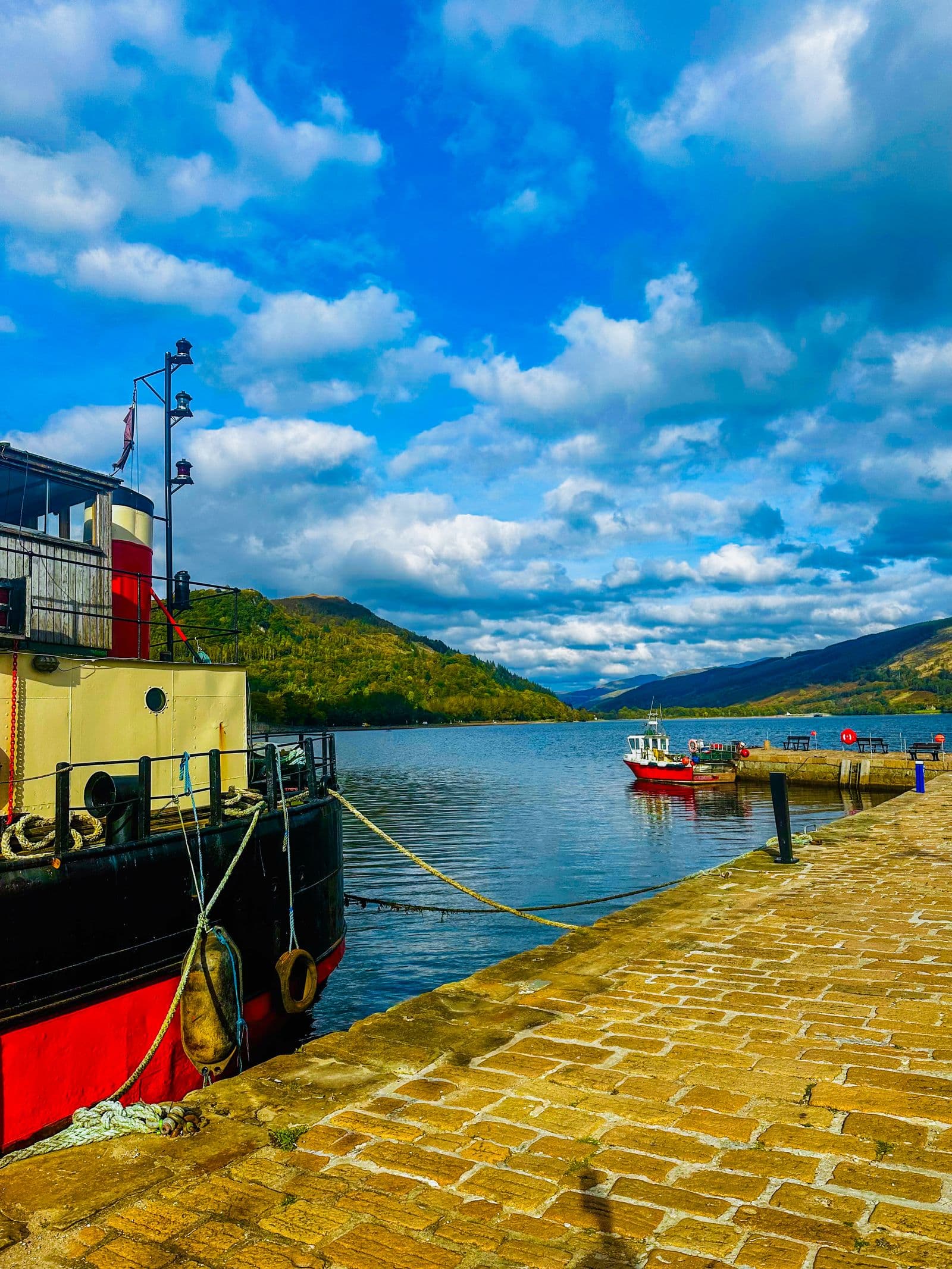 A red and black steamer moored at a Scottish loch pier under a wide cloudy sky