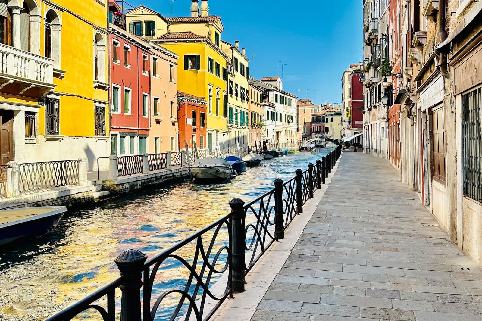 A Venetian canal lined with yellow, orange and cream houses under a bright sky
