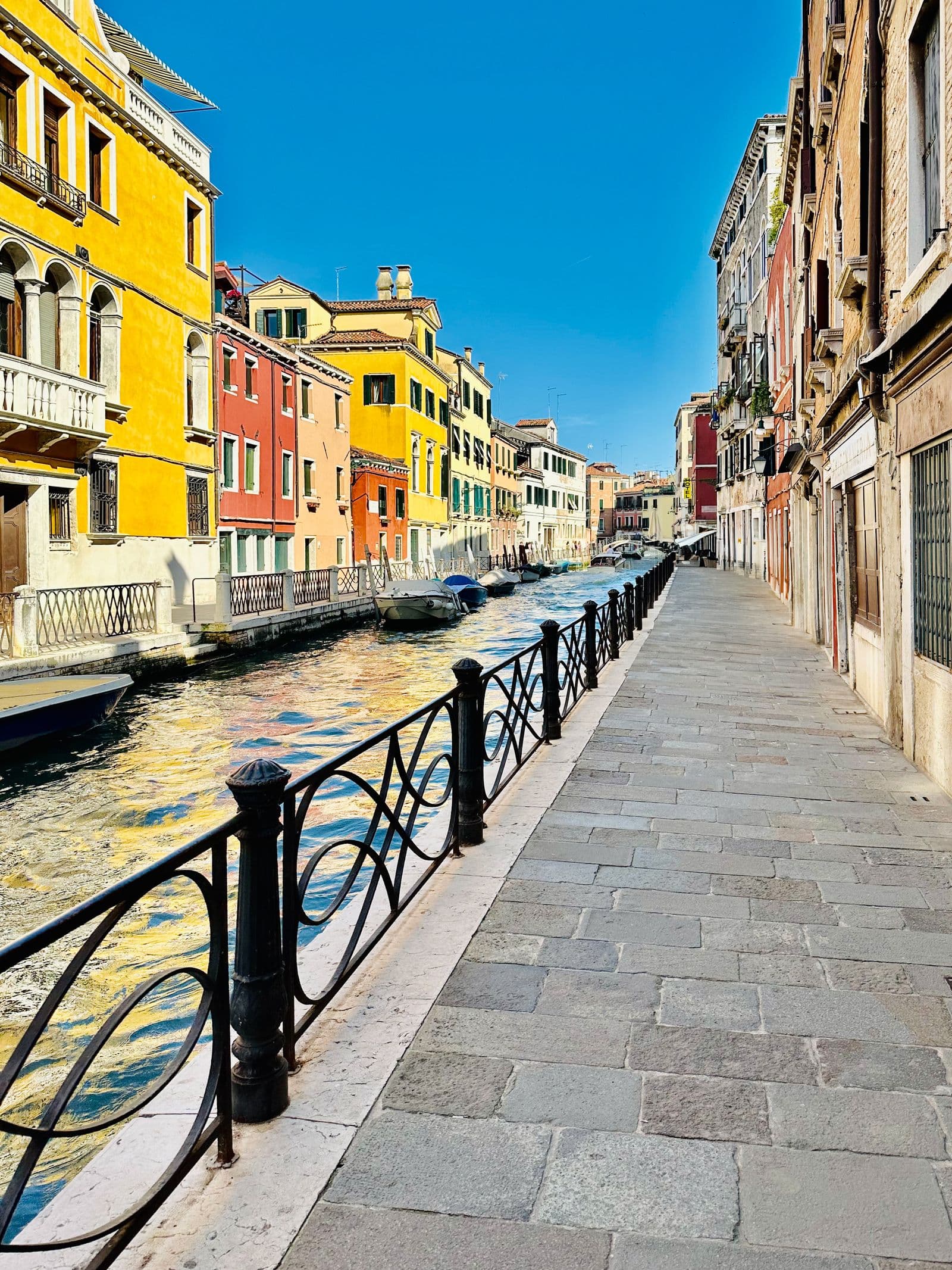 A Venetian canal lined with yellow, orange and cream houses under a bright sky